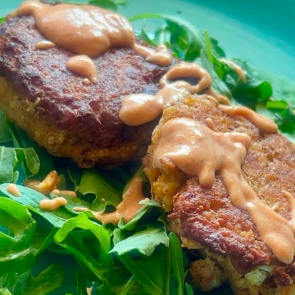 A seared patty with a sauce drizzle over greens.