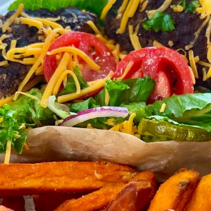 Loaded burger with shredded cheese and tomato beside sweet potato fries
