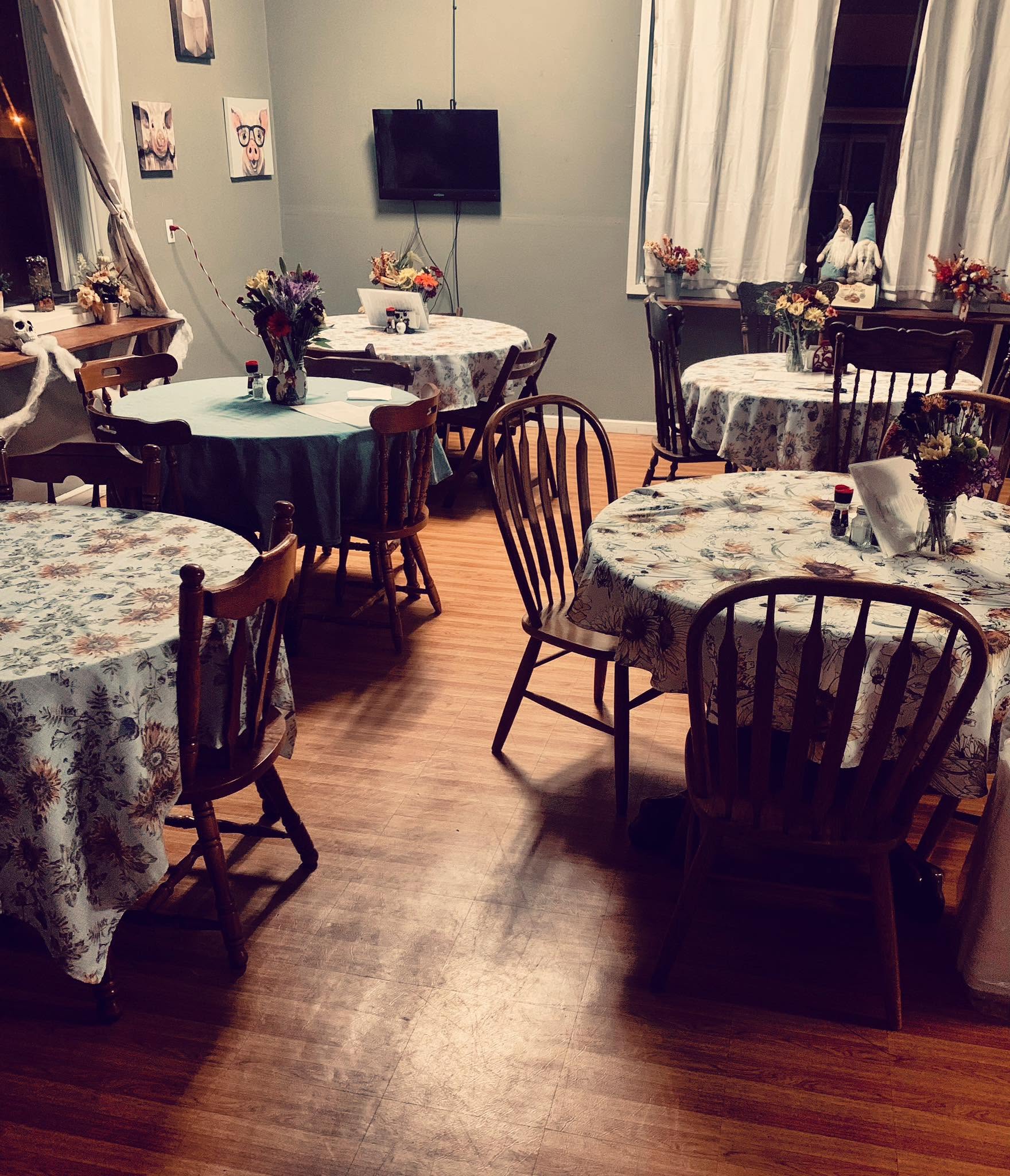 Cafe dining room with floral tablecloths, wooden spindle chairs and jars of wildflowers on set tables